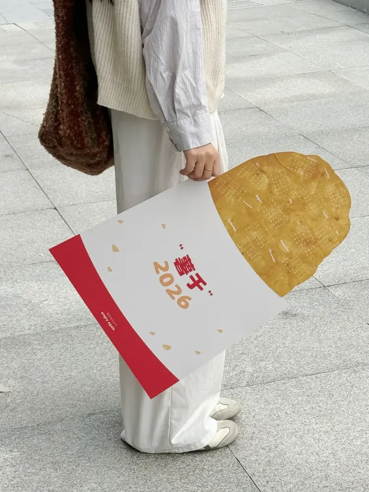 原创作者实拍：手持薯饼形年历与食物纸套。